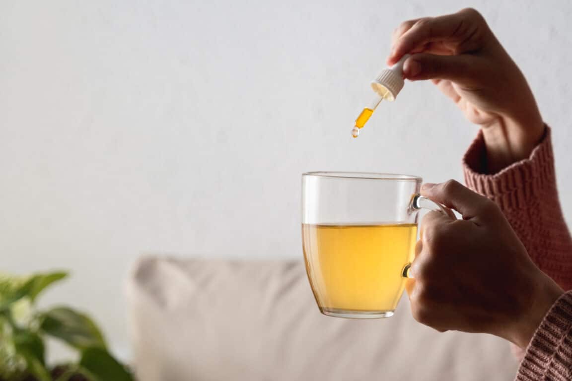 jeune femme versant quelques gouttes d'huile de CBD dans son infusion