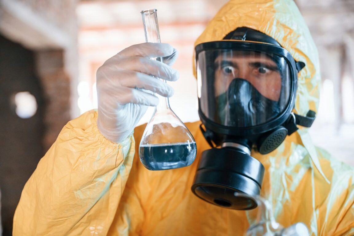 Scientifique en combinaison de protection examinant un liquide dans un flacon.