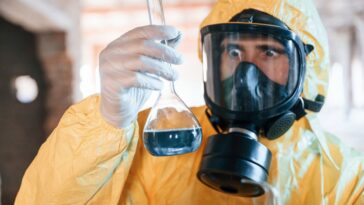 Scientifique en combinaison de protection examinant un liquide dans un flacon.